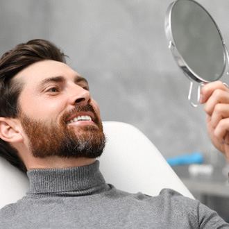A man looking at his smile in the mirror at the dentist