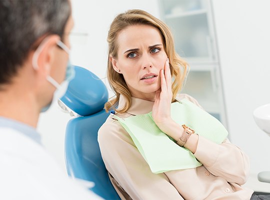 Woman in dental chair holding jaw