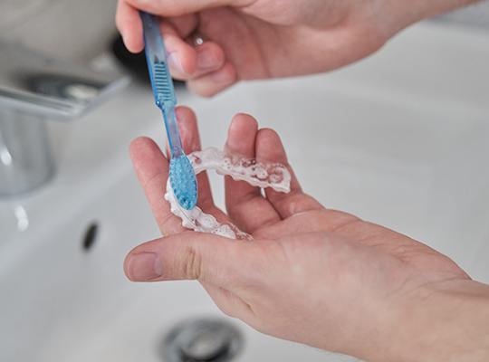 Patient cleaning clear aligner in sink
