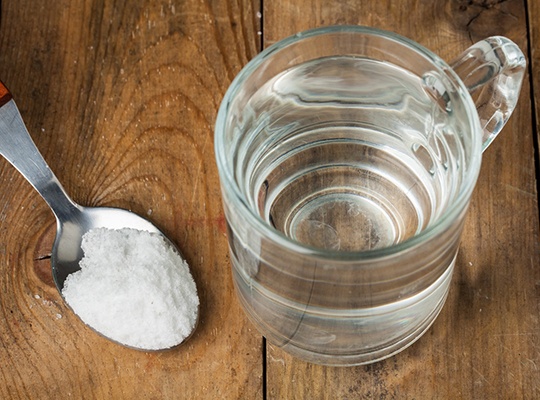 Spoonful of salt next to glass of water