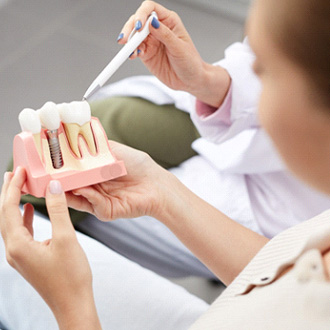 Dentist pointing to sample dental implant with white pen