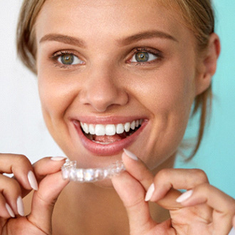 Smiling woman about to put Invisalign over upper arch