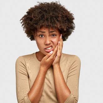 Woman in taupe shirt holding hands to jaw in pain