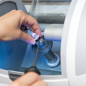 Hands taking CEREC crown out of milling machine