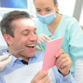 Man in dental chair smiling at results with dentist looking over shoulder