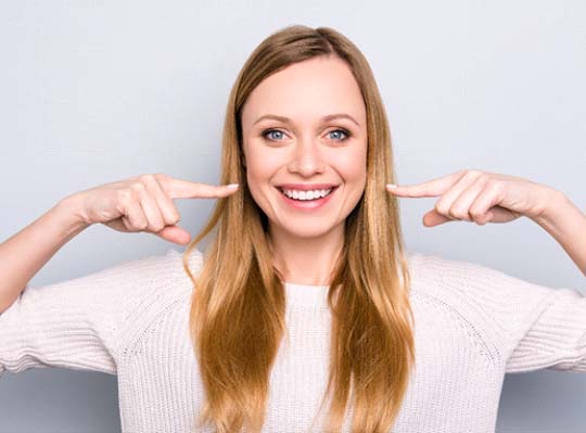 Woman pointing to her smile on white background