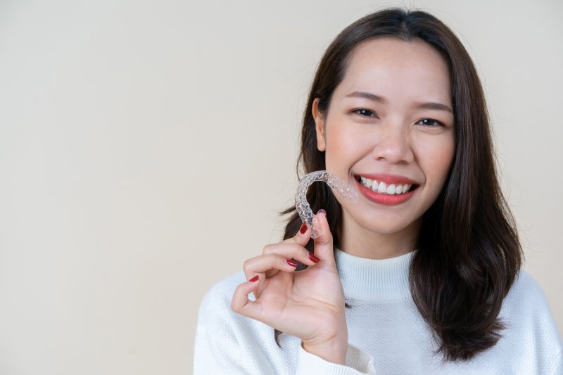 person holding Invisalign aligner and smiling