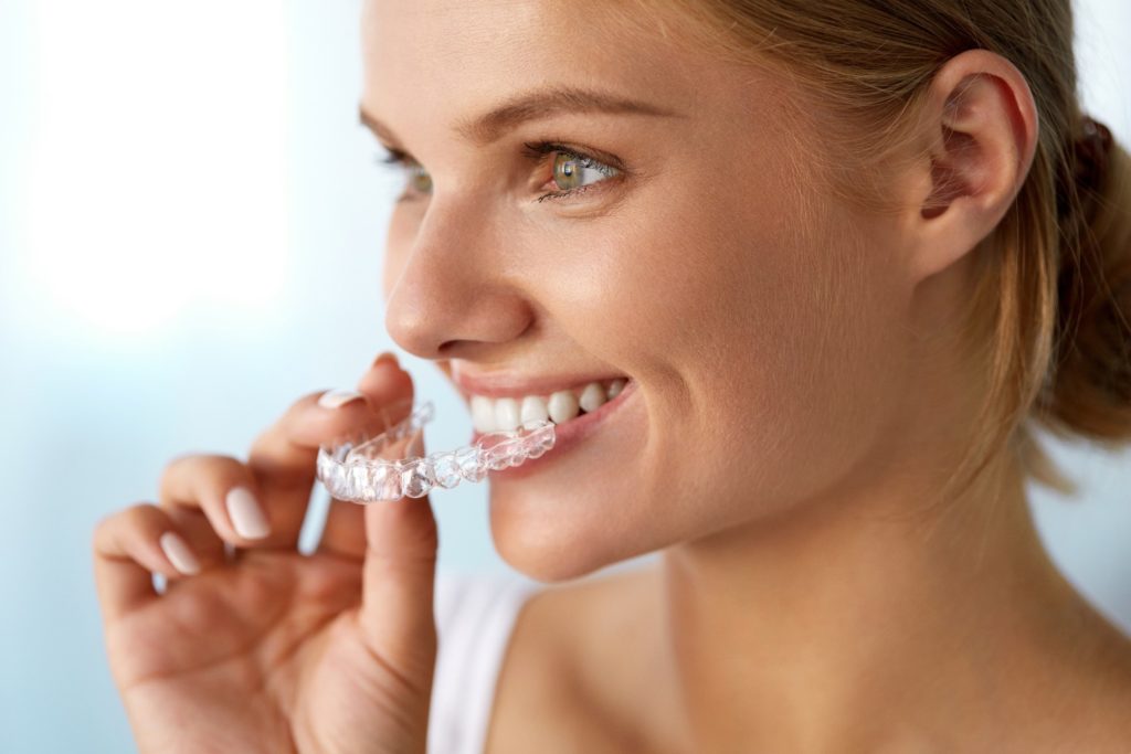 Woman smiling while putting on Invisalign aligners